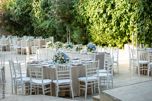 Elegant outdoor wedding reception with round tables, white chairs, and floral centerpieces