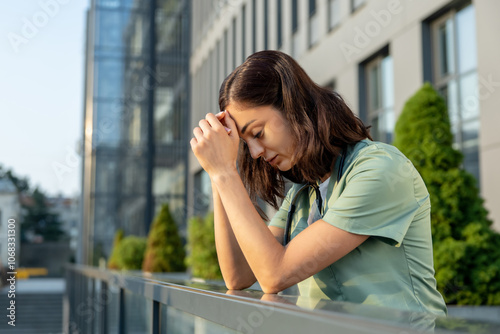 Young female doctor standing near clinic and feeling tired