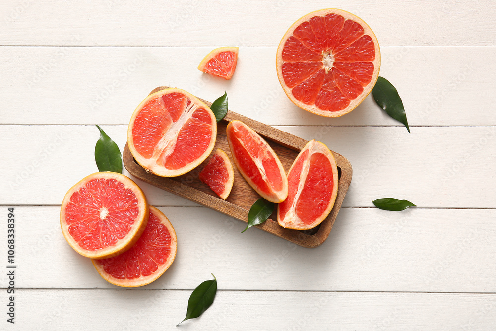 Tray with cut fresh grapefruit and leaves on white wooden background