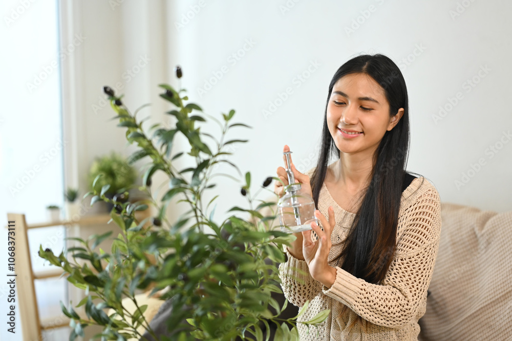 Charming young woman watering her indoor plant Charming young woman watering her indoor plant