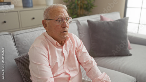 Mature, grey-haired man wearing glasses seated in a cozy living room with relaxed decor. photo