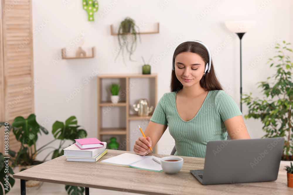 Student in headphones studying at wooden table indoors Student in headphones studying at wooden table indoors