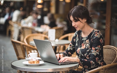 A young woman works on her laptop while sitting at an outdoor cafe table.