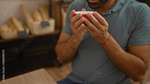 Young man enjoying a warm beverage in a cozy bakery filled with fresh bread, illustrating a serene moment indoors.