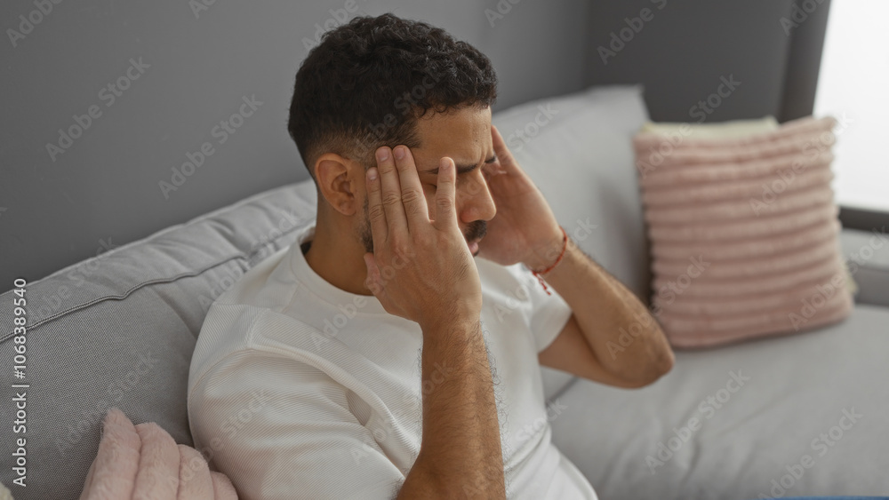 Young man in living room holding his temples looking stressed sitting on a sofa Young man in living room holding his temples looking stressed sitting on a sofa