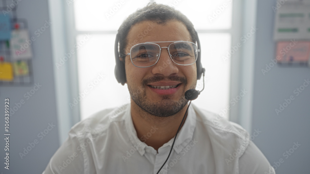 Young man with glasses and headset smiling in an indoor office setting, showcasing a friendly and professional work environment. Young man with glasses and headset smiling in an indoor office setting, showcasing a friendly and professional work environment.