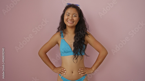 Obraz na plátně Young chinese woman in a blue bikini smiling confidently over a pink background
