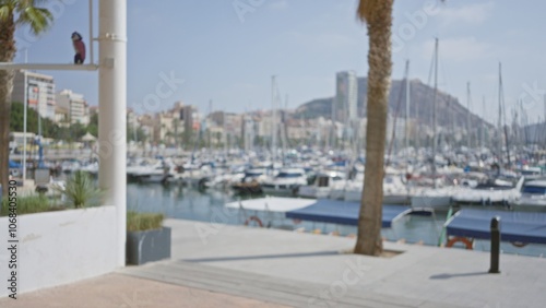 Blurred marina view with boats docked, city skyline in background, palm trees, bright sky, and walking path creating a defocused vibrant outdoor urban scene photo