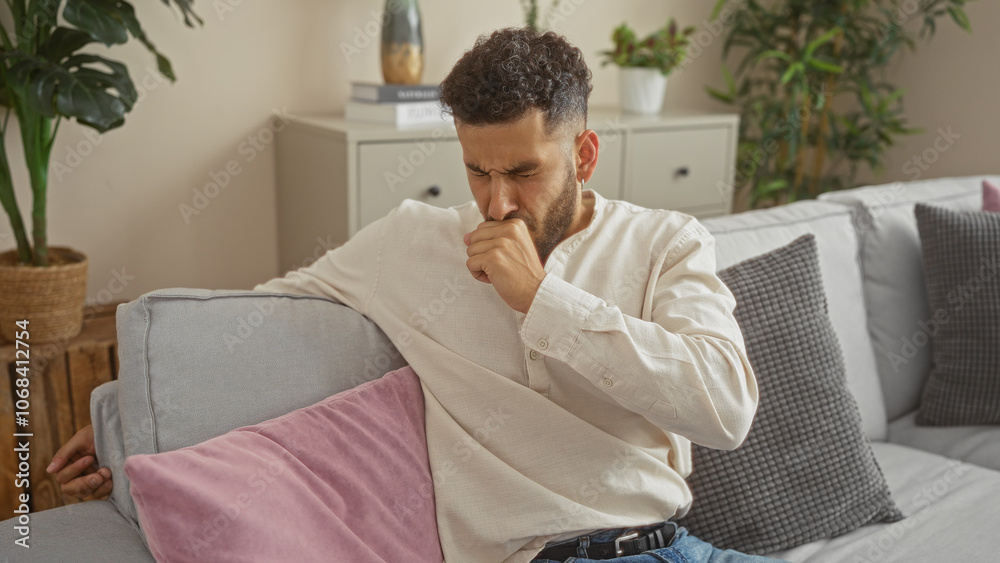 A young hispanic man coughs while sitting on a couch in an apartment living room, highlighting an indoor setting with houseplants and cushions. A young hispanic man coughs while sitting on a couch in an apartment living room, highlighting an indoor setting with houseplants and cushions.