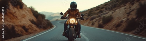 A man is riding a motorcycle down a road. The road is empty and the man is wearing a leather jacket