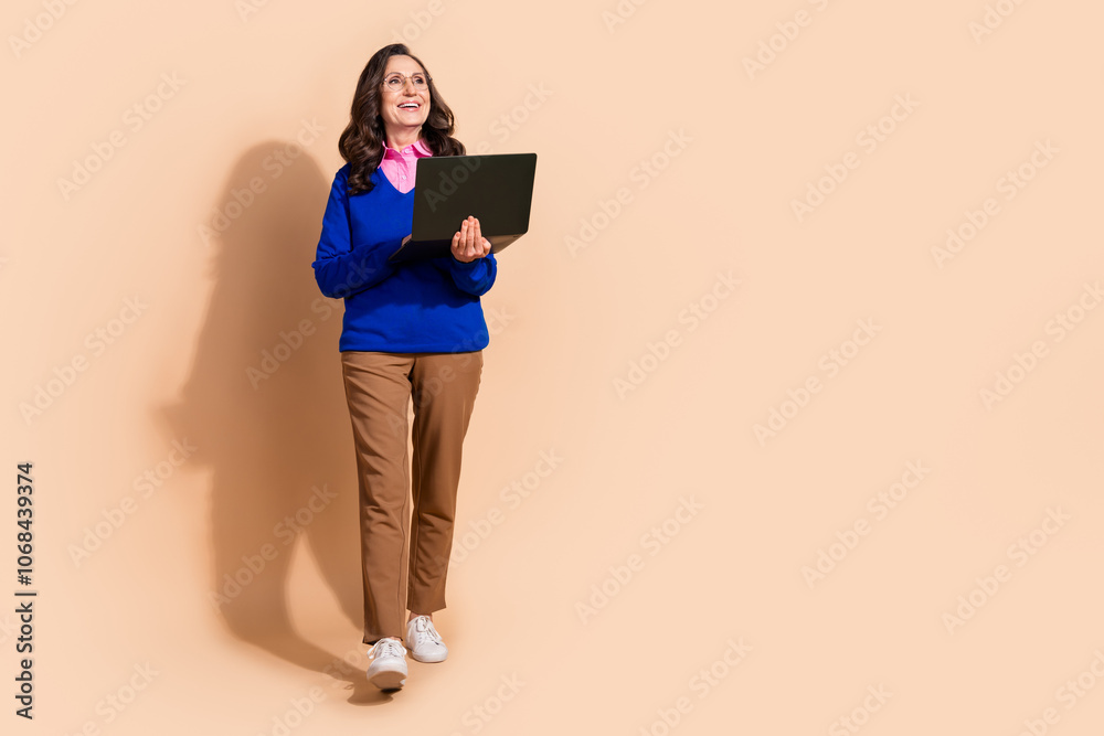 Photo of cheerful lovely retired woman wear blue stylish clothes hold device look empty space isolated on beige color background Photo of cheerful lovely retired woman wear blue stylish clothes hold device look empty space isolated on beige color background