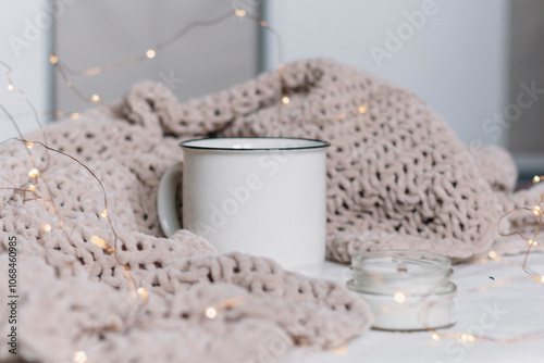 Obraz na płótnie A white ceramic mug and a candle in a glass jar with a wooden wick stand among a knitted plush soft warm plaid. Warm comfort w salonie