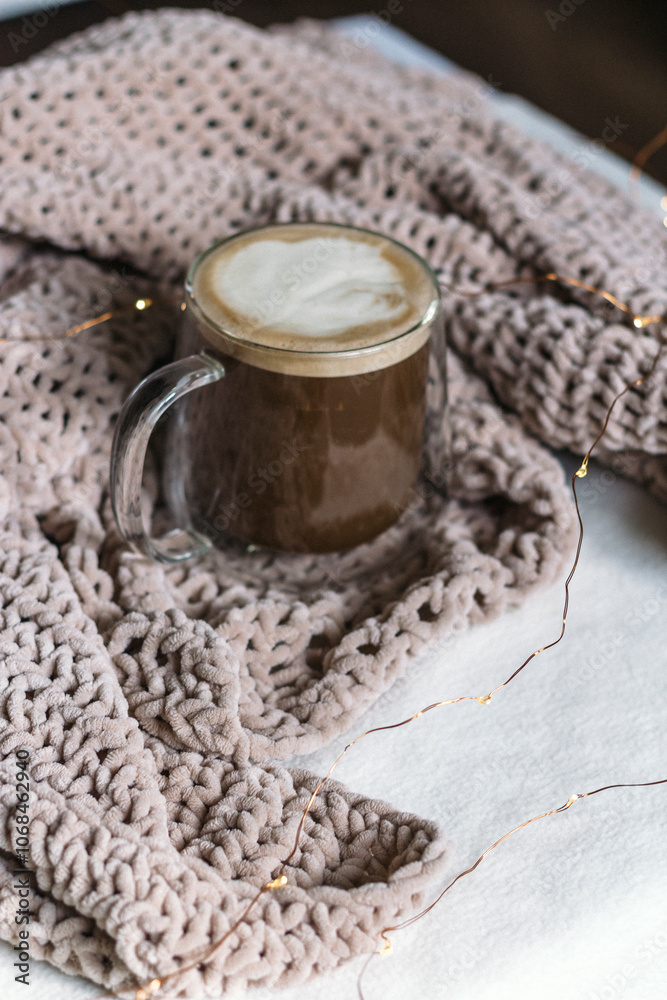 A cozy still life. Black coffee with milk in a glass mug on the table in a warm beige knitted plaid. Place for the text