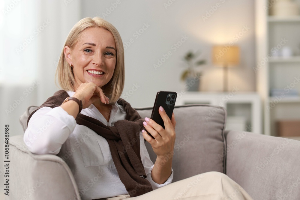 Smiling middle aged woman with smartphone on armchair at home Smiling middle aged woman with smartphone on armchair at home