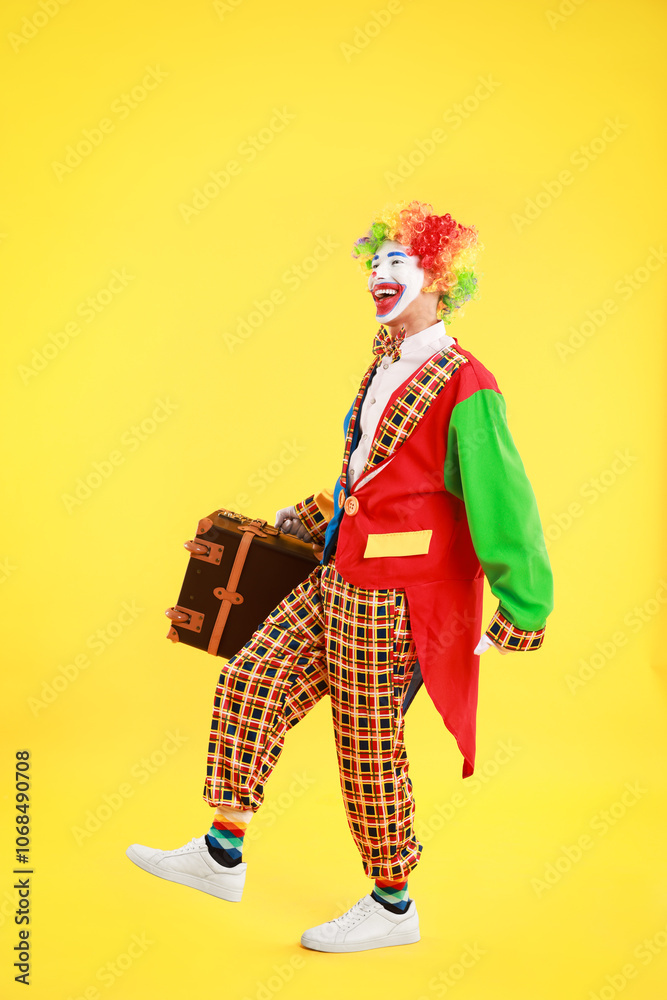 Happy clown with suitcase on yellow background
