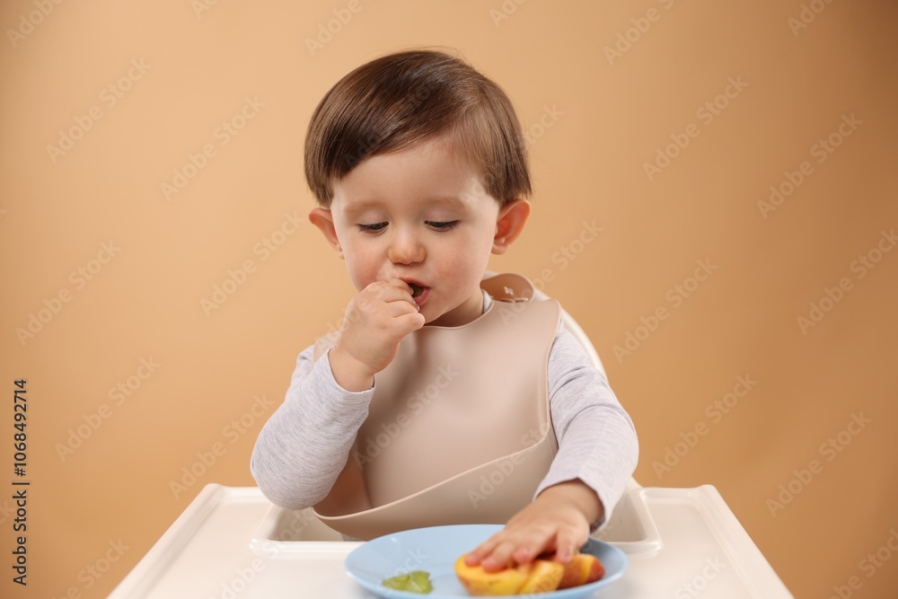 Healthy baby food. Cute little kid eating fruits in high chair on beige background Healthy baby food. Cute little kid eating fruits in high chair on beige background