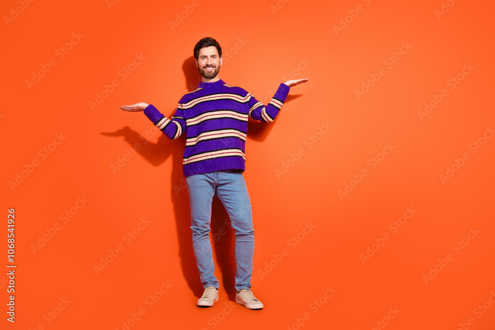 Full size photo of nice young male compare hold empty space wear trendy striped violet outfit isolated on orange color background Full size photo of nice young male compare hold empty space wear trendy striped violet outfit isolated on orange color background