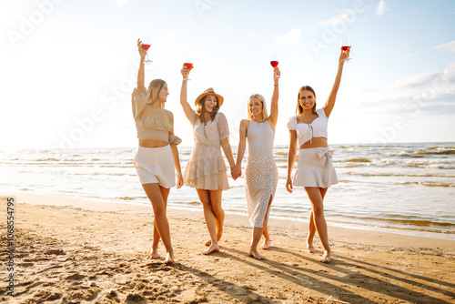 Canvas Print Happy women with glasses of wine walking on the beach