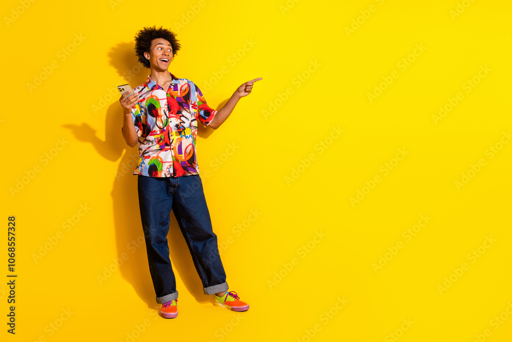 Full size photo of nice young man phone direct finger empty space wear shirt isolated on bright yellow color background Full size photo of nice young man phone direct finger empty space wear shirt isolated on bright yellow color background