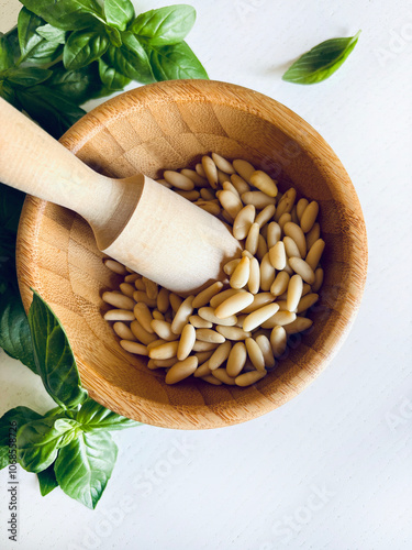 Mortaio di legno con pinoli e foglie di basilico fresco su fondo di legno bianco. Direttamente sopra.