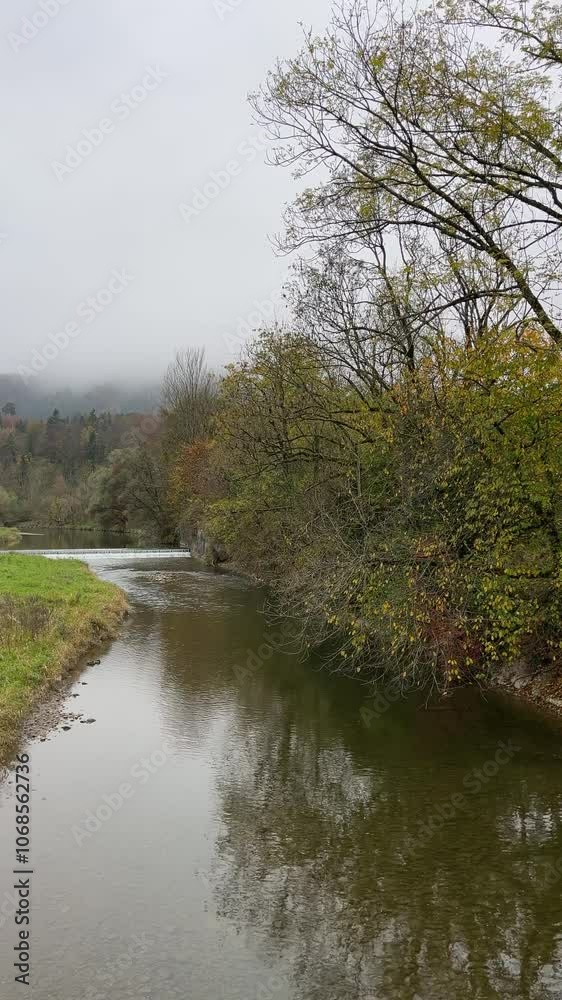 Calm shallow river with colorful autumn trees on the banks on a dark foggy day. Sihl river in Zurich, Switzerland. Calm shallow river with colorful autumn trees on the banks on a dark foggy day. Sihl river in Zurich, Switzerland.