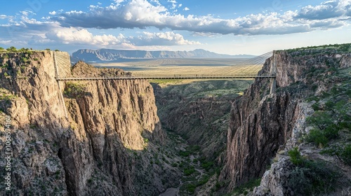 A suspension bridge stretches across a deep canyon with a river winding through the valley below.