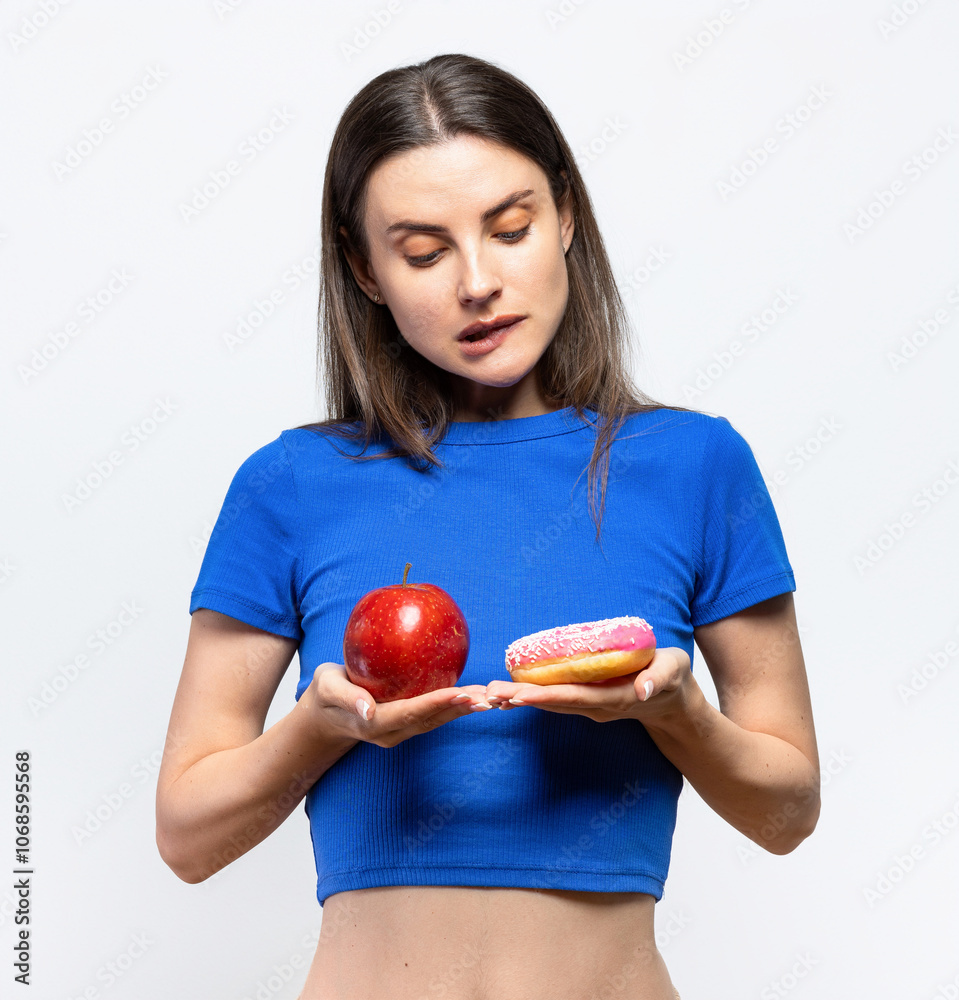 Beautiful young woman having to choose in between a donut and a red apple. On white background Beautiful young woman having to choose in between a donut and a red apple. On white background