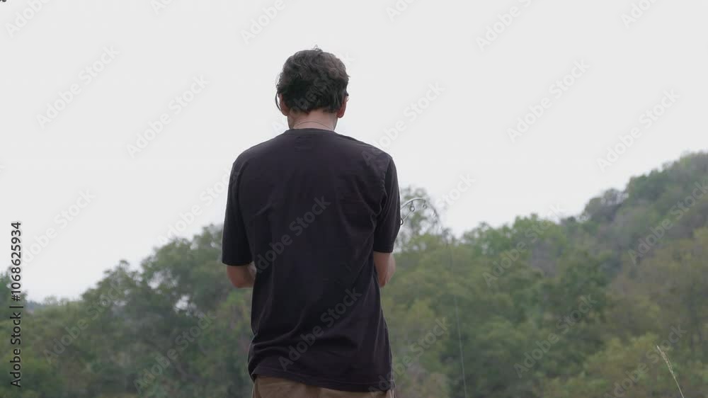 A young man reels in his fishing line, the pole bending dramatically under the weight of his catch. A young man reels in his fishing line, the pole bending dramatically under the weight of his catch.