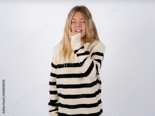 caucasian teen girl wearing striped knitted sweater over white feeling unwell and coughing as symptom for cold or bronchitis. Healthcare concept.