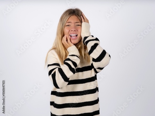 Doleful desperate crying caucasian teen girl wearing striped knitted sweater over white , looks stressfully, frowns face, feels lonely and anxious photo