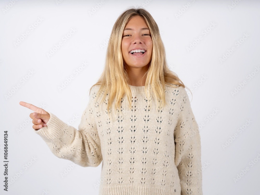 caucasian teen girl wearing knitted sweater over white laughs happily points away on blank space demonstrates shopping discount offer, excited by good news or unexpected sale.