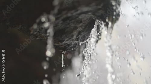 Clear droplets drip from rocky ledges in slow motion, each one distinct. Behind, a spring waterfall flows, representing peace and water scarcity issues.