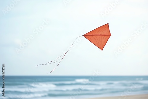 Orange kite flying against blue sky above sea horizon