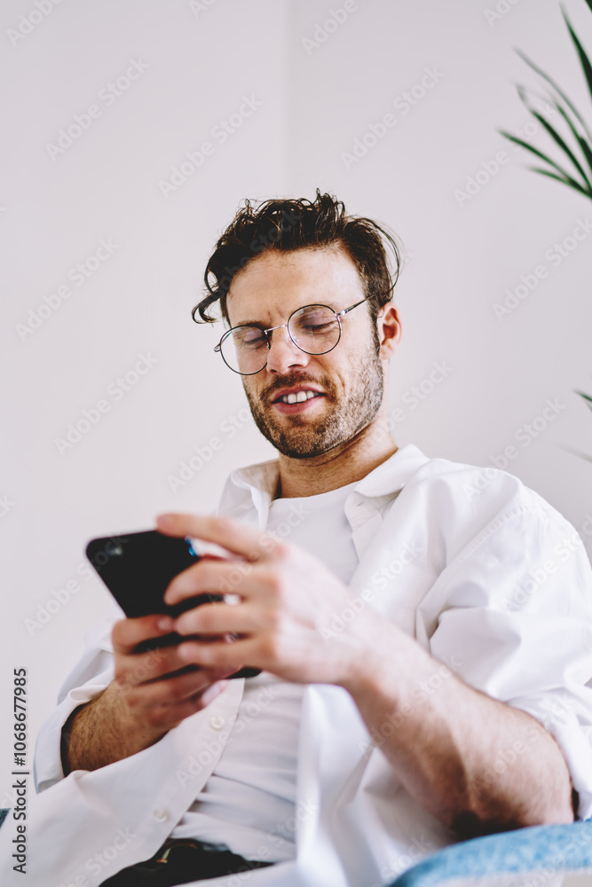 Smiling male texting on cellphone in room Smiling male texting on cellphone in room