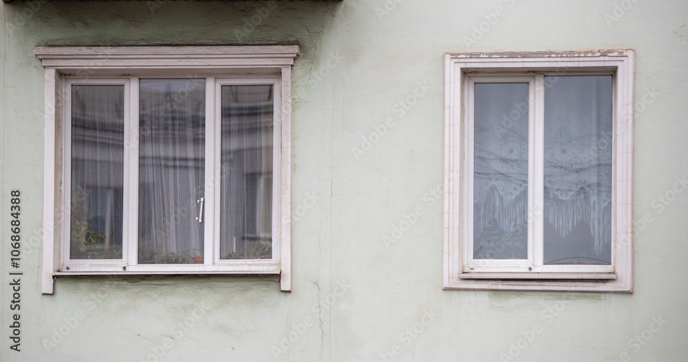 Two windows with white curtains and a white wall Two windows with white curtains and a white wall