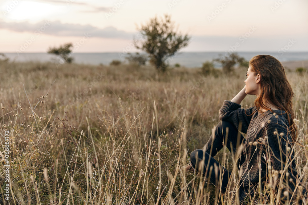 Peaceful woman sitting in a sunlit field gazing at the vast expanse of the ocean Peaceful woman sitting in a sunlit field gazing at the vast expanse of the ocean