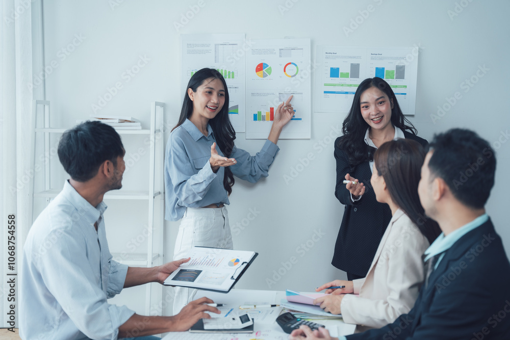 Fototapeta premium Team Meeting: A diverse team of Asian business professionals engaged in a productive meeting, analyzing data and collaborating on strategies. The image embodies the spirit of modern business.