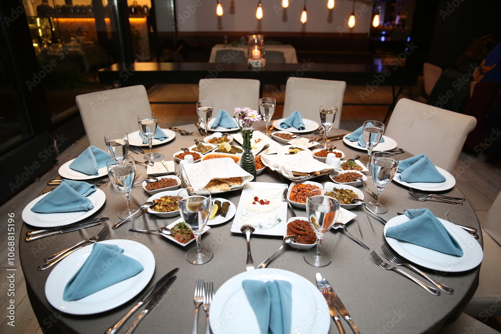An elegant dinner table setting with a minimalist design. The table is decorated with blue napkins, white plates, and simple glassware An elegant dinner table setting with a minimalist design. The table is decorated with blue napkins, white plates, and simple glassware