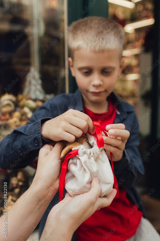 Cute little boy with his mother near the Christmas toy shop. Funny happy child opens a box with a gift on the background of a shop window. Holidays, Christmas, childhood and people concept Cute little boy with his mother near the Christmas toy shop. Funny happy child opens a box with a gift on the background of a shop window. Holidays, Christmas, childhood and people concept