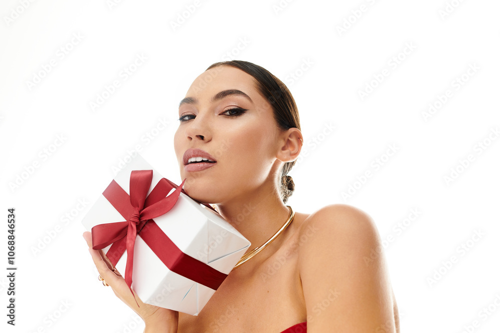 A young beautiful woman smiles as she playfully holds a gift adorned with a red ribbon. A young beautiful woman smiles as she playfully holds a gift adorned with a red ribbon.