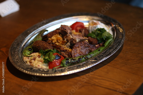 A traditional Turkish mixed grill, served on a silver platter. The dish is a colorful and flavorful combination of grilled meats, vegetables, and rice