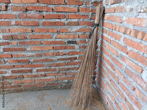 A broom stick lies in the corner of the room against the background of a red brick wall photo