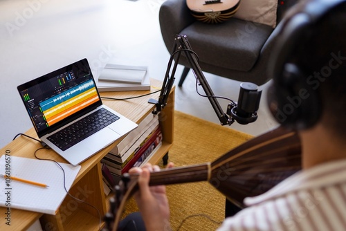 A musician is captured recording music in a home studio setup, with a microphone and a laptop displaying sound editing software photo