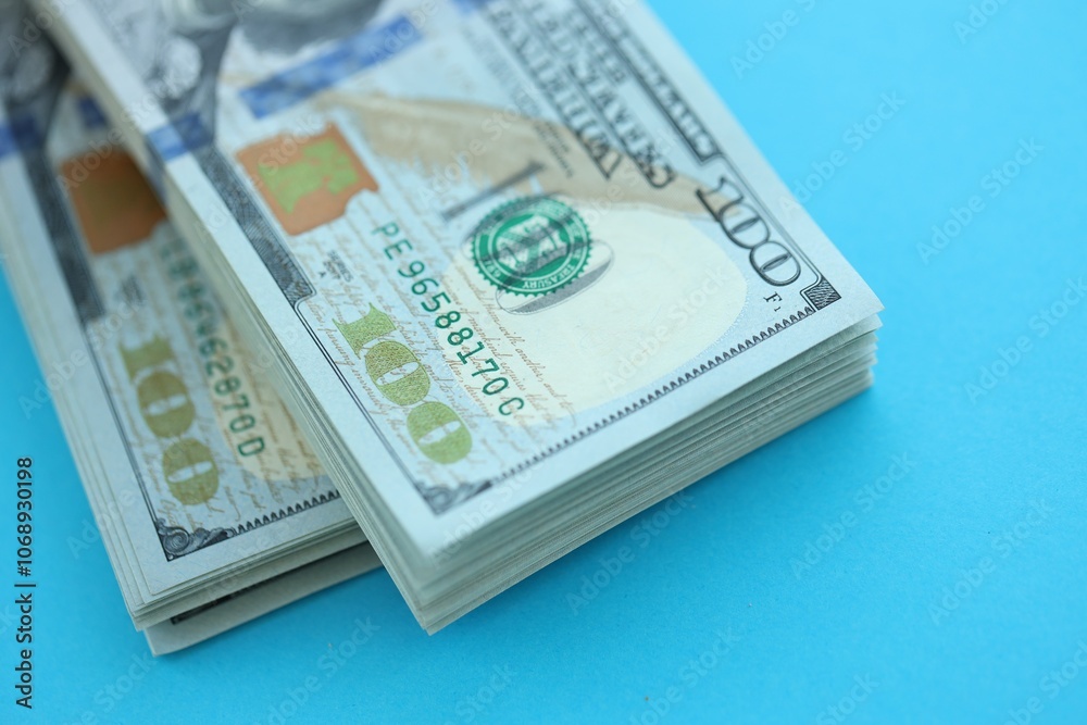 Big amount of hundred dollar bills in thick stack lies on bright blue color paper background Big amount of hundred dollar bills in thick stack lies on bright blue color paper background