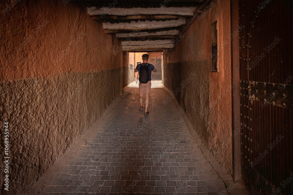 Young Adult Casual Attire male person walking and exploring a narrow medina alleyway street tunnel in famous old Medina, Marrakech, Morocco, authentic rustic textured walls and atmospheric shadows, Young Adult Casual Attire male person walking and exploring a narrow medina alleyway street tunnel in famous old Medina, Marrakech, Morocco, authentic rustic textured walls and atmospheric shadows,