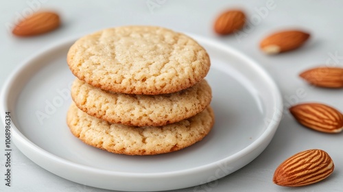 Three almond cookies stacked on a small white plate with almonds scattered around.