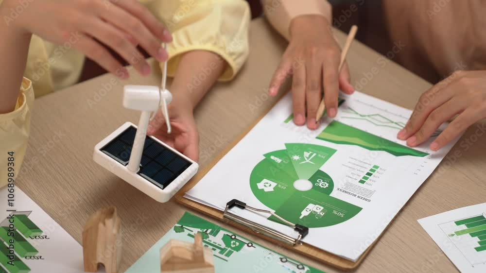 Business team analyze green power graph usage. Coworker with windmill model represented using clean energy and wooden block symbolized eco house choosing way to decrease carbon in future. Delineation. Business team analyze green power graph usage. Coworker with windmill model represented using clean energy and wooden block symbolized eco house choosing way to decrease carbon in future. Delineation.