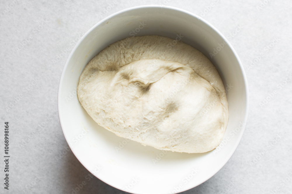 Overhead view of challah dough in a white mixing bowl, top view of homemade challah dough resting in a white mixing bowl, process of making challah Overhead view of challah dough in a white mixing bowl, top view of homemade challah dough resting in a white mixing bowl, process of making challah