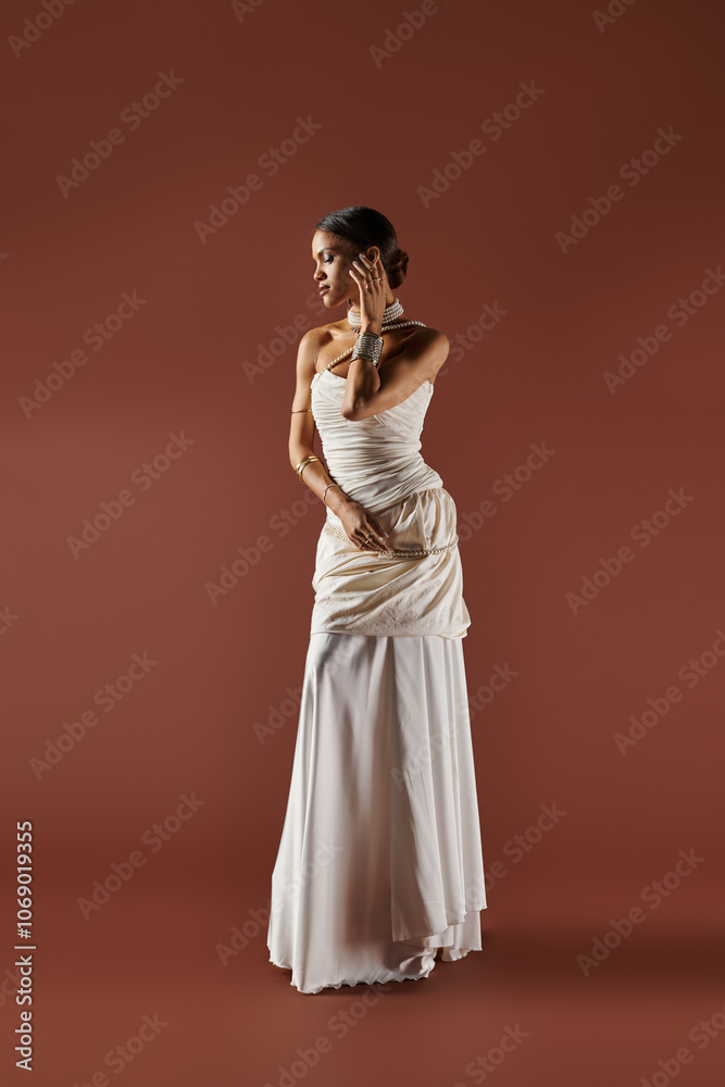 A beautiful African American woman showcases grace wearing a white dress and a pearl necklace in a studio.