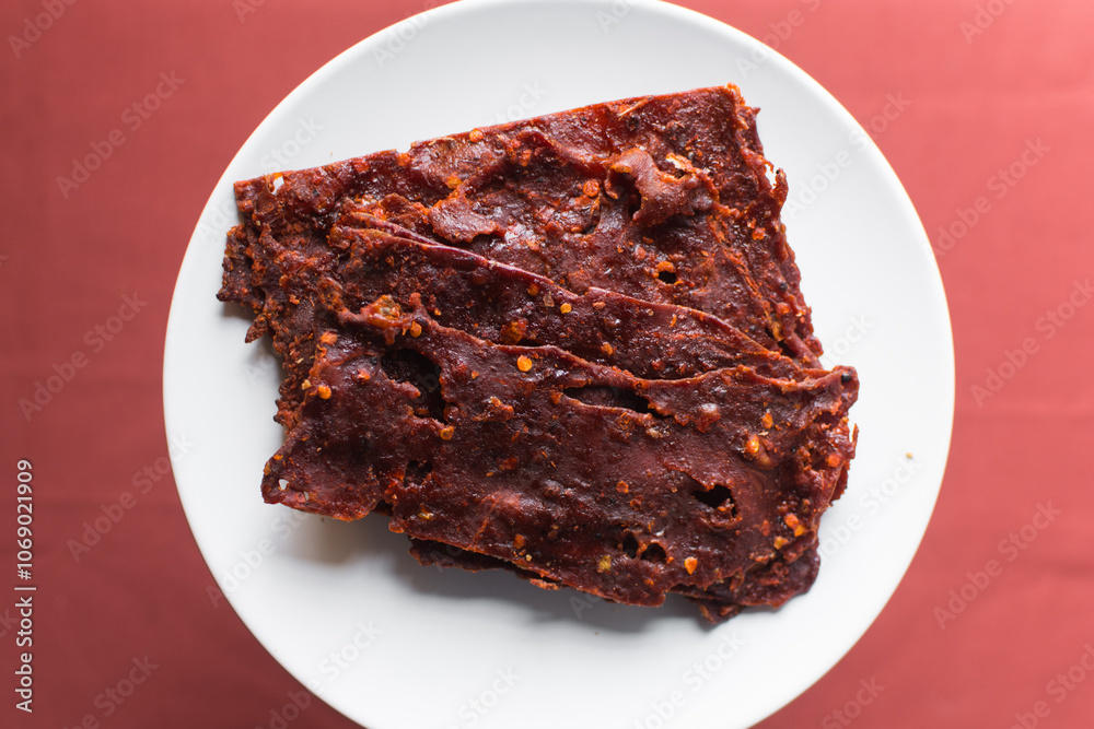 Overhead view of Nigerian kilishi on a white plate, top view of nigerian spicy beef jerky, flatlay of dried beef suya Overhead view of Nigerian kilishi on a white plate, top view of nigerian spicy beef jerky, flatlay of dried beef suya